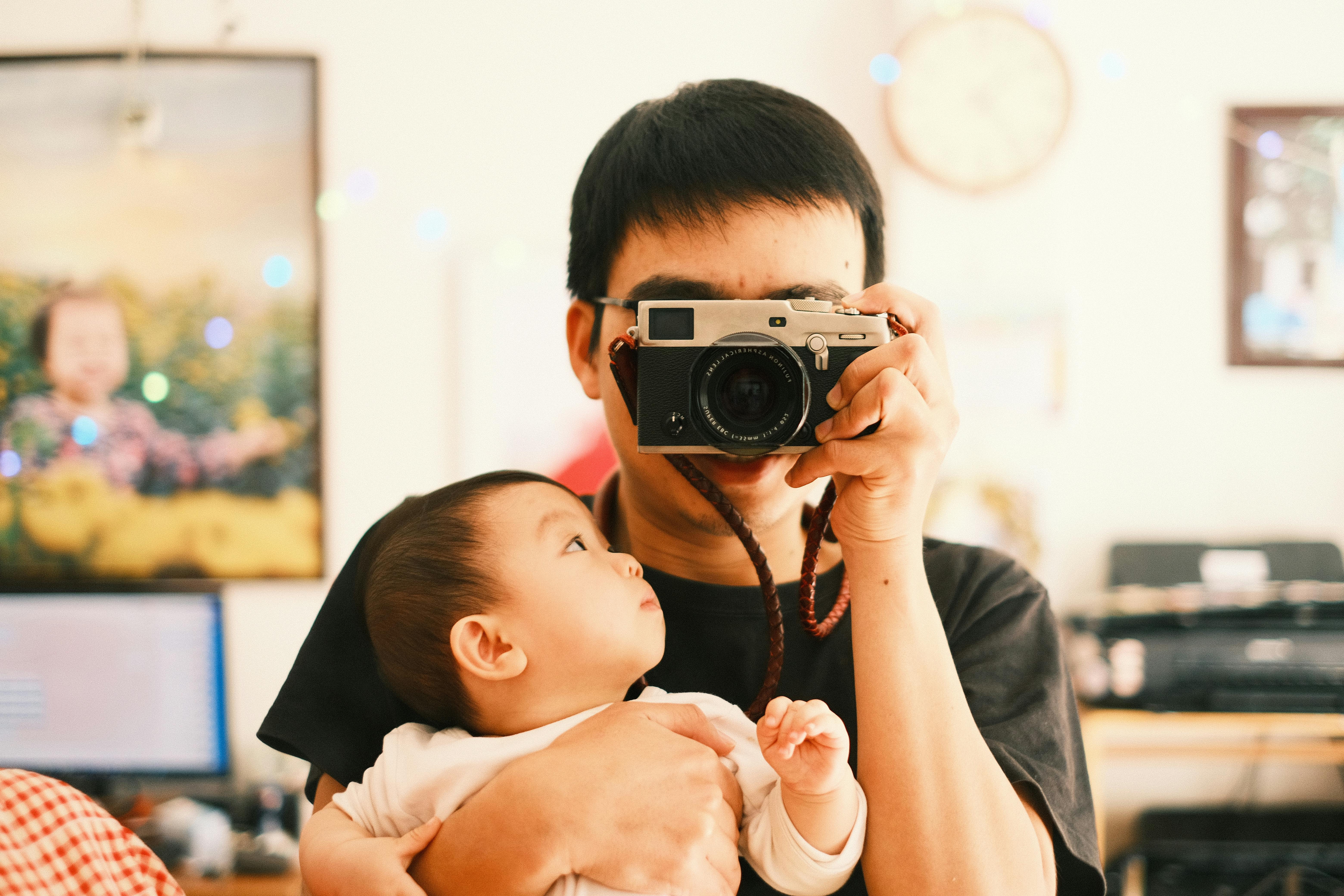 Father with baby captures a moment with a camera, indoors.